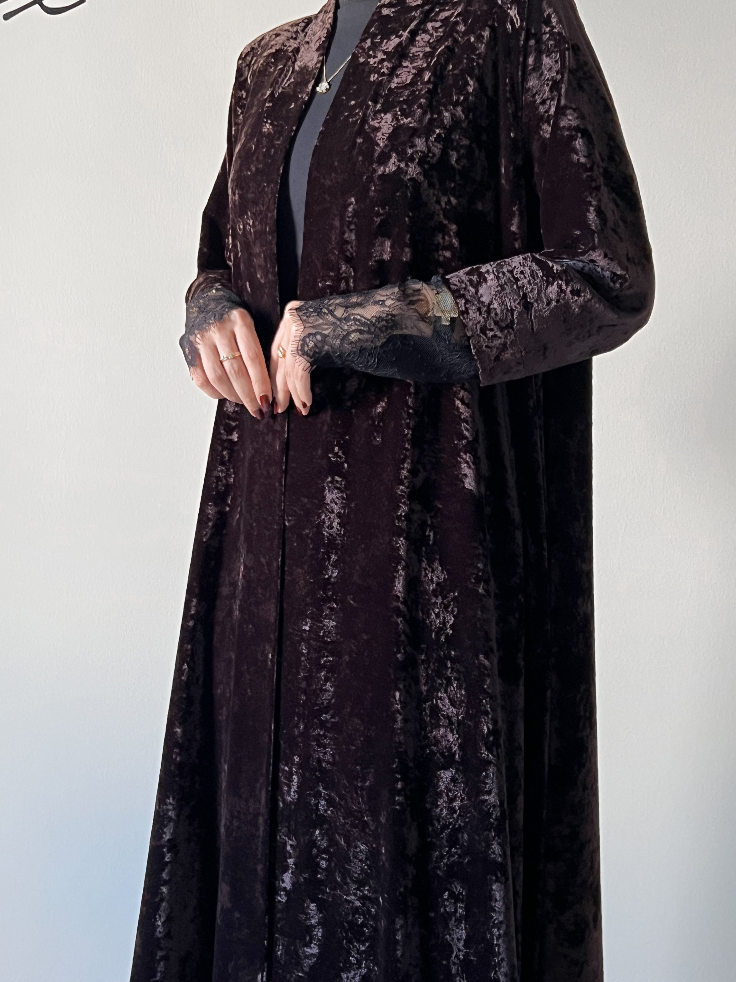 An elegant black abaya crafted from soft velvet fabric, finished with delicate lace detailing on the sleeves for a timeless and feminine look.